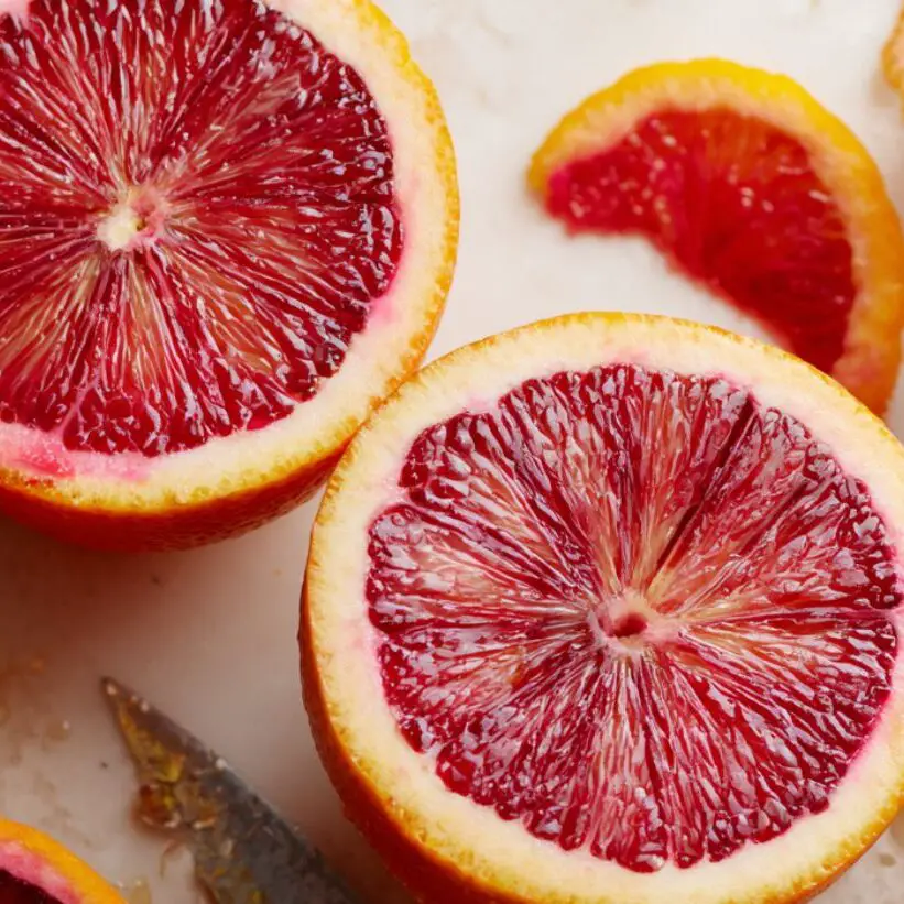 Freshly halved blood oranges with juice droplets and peels on a white kitchen counter.


