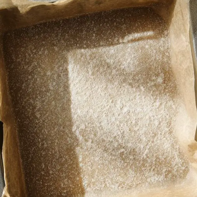 8x8 inch baking pan lined with parchment paper on white kitchen counter.
