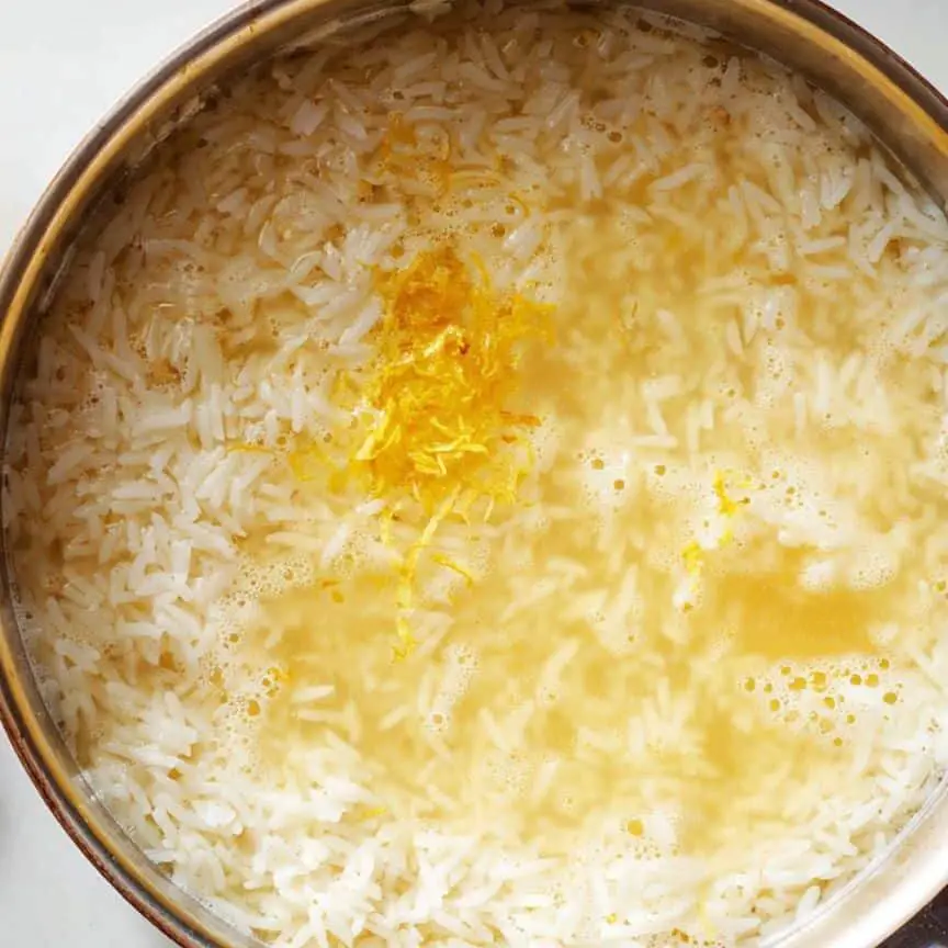 Adding lemon juice and broth to rice in a saucepan.