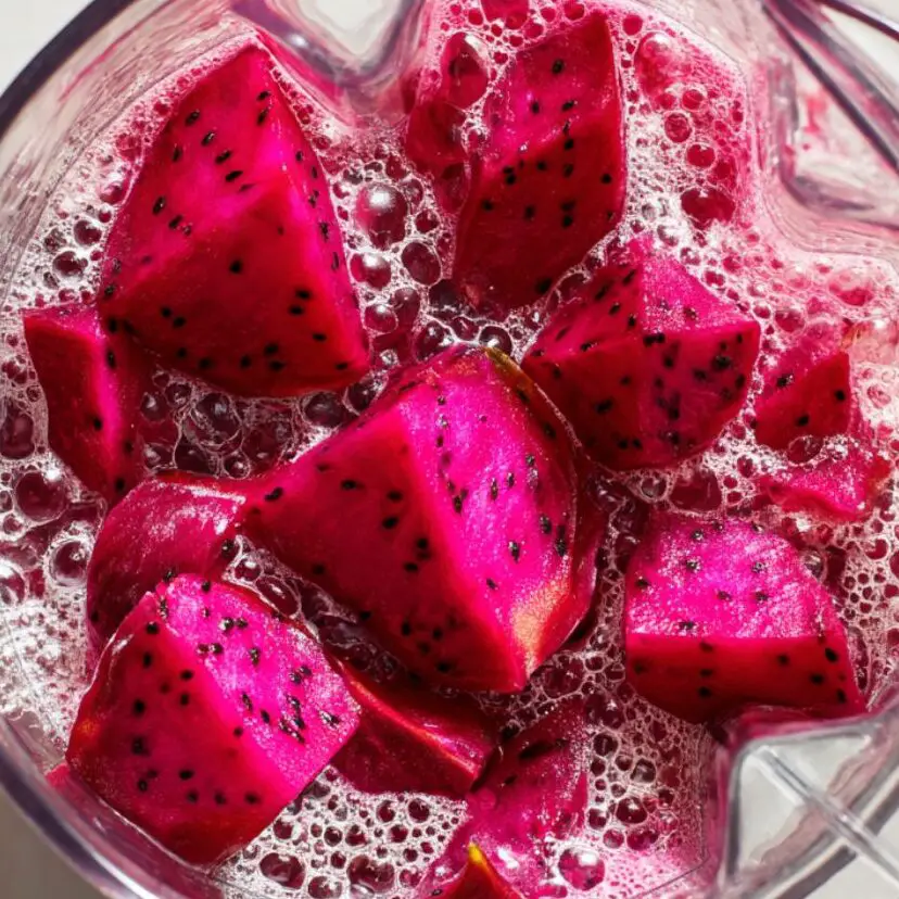 Dragon fruit chunks blending in a blender with water on a white kitchen counter.