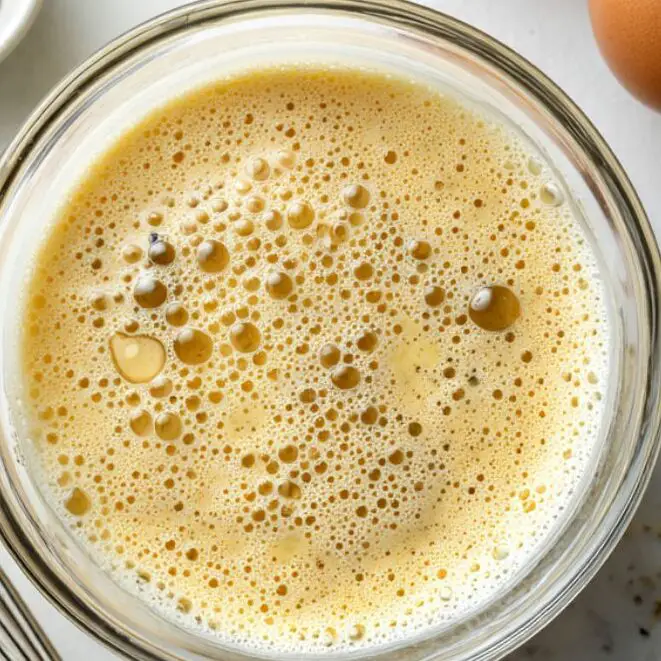 Whisked eggs with milk and seasoning in a glass bowl.