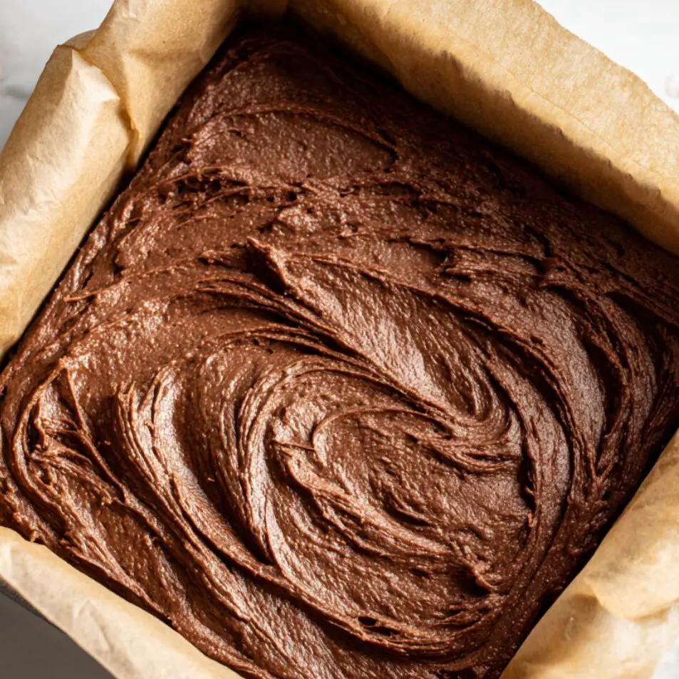 Thick chocolate brownie batter being spread in the prepared pan.