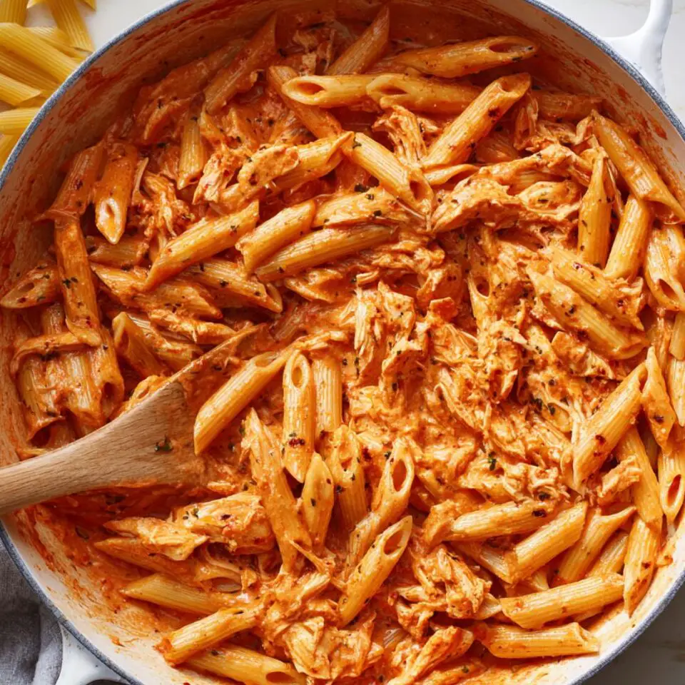 Pasta and chicken stirred into creamy sauce in a white pan