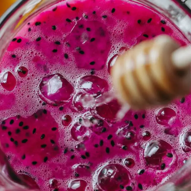 Lemon juice and honey being added to the dragon fruit base in a glass pitcher.