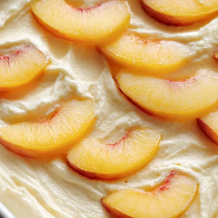 Batter in pan topped with fresh peach slices on white counter.