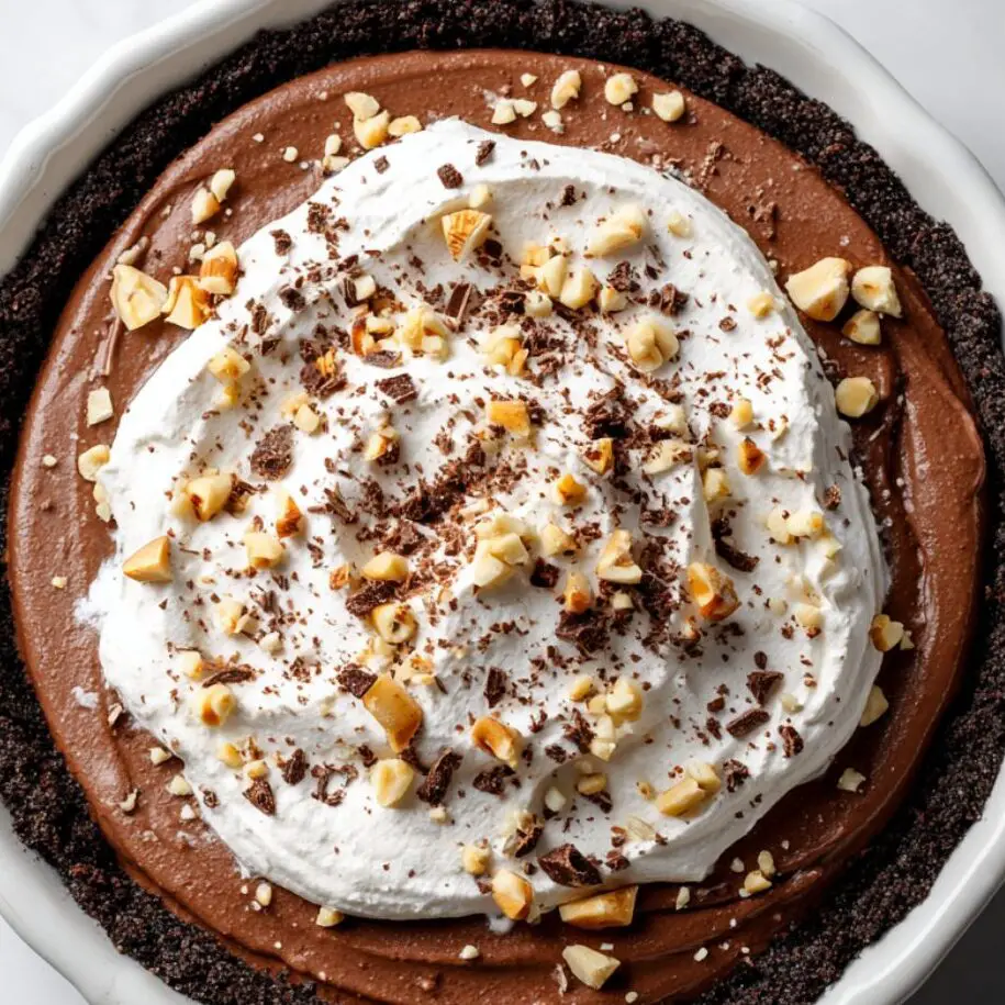 Nutella pie filling being spread into Oreo crust, topped with whipped cream and chocolate shavings.