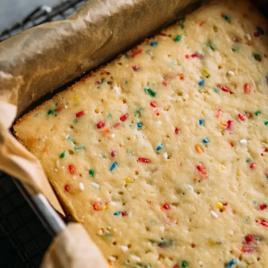 Freshly baked Funfetti bars in a parchment-lined pan cooling on a rack

