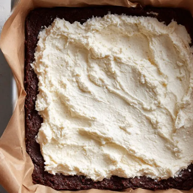 Smooth cheesecake mixture being poured or spread over brownie layer.