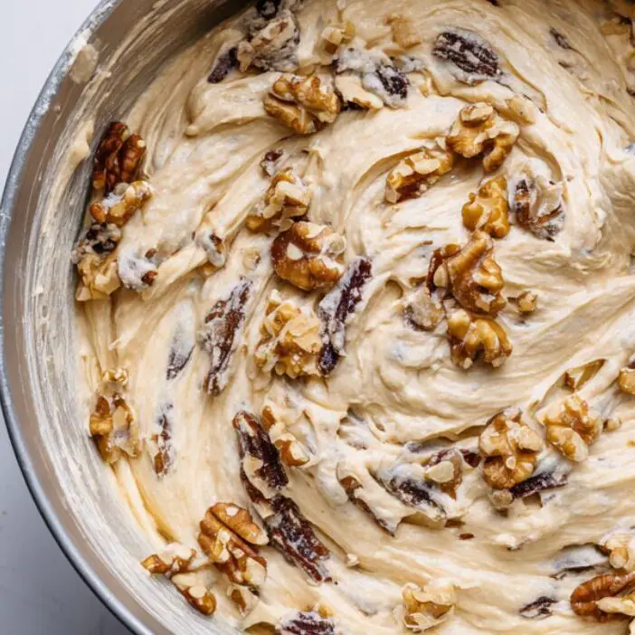 A bowl of date and walnut cake batter being folded, with walnuts and dates visible in the mix.

