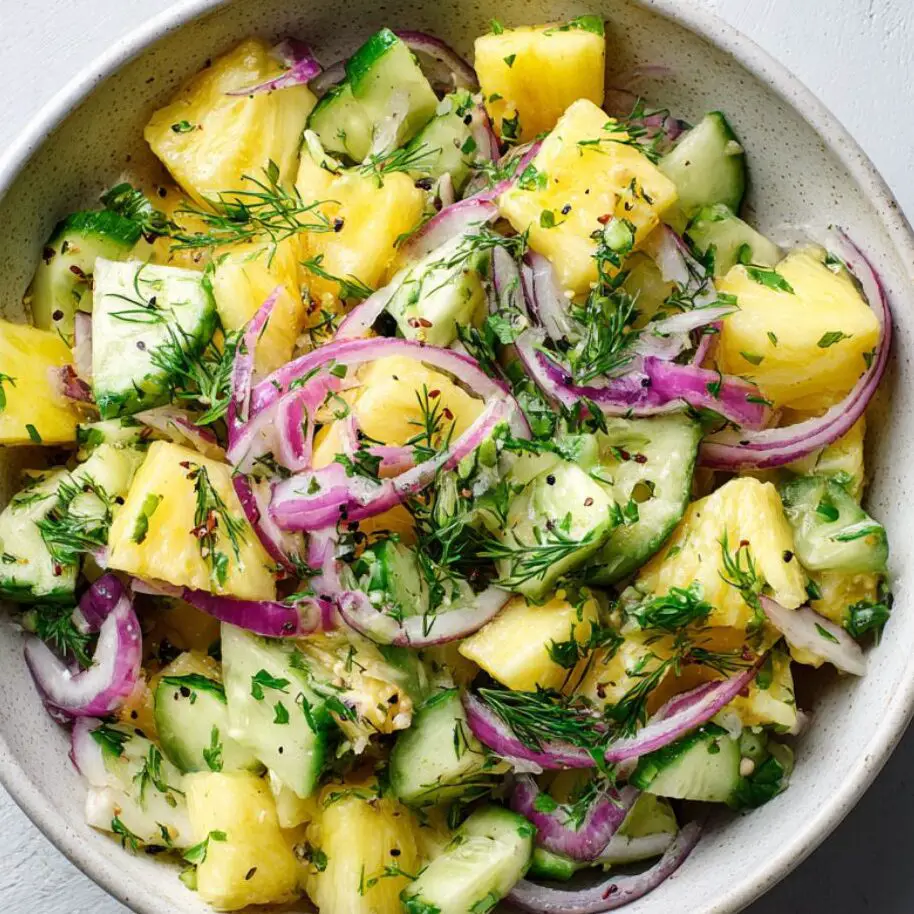 Tossed pineapple cucumber salad with herbs in a large white bowl

