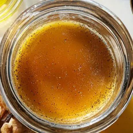 Small jar of vinaigrette with ingredients nearby on the counter.