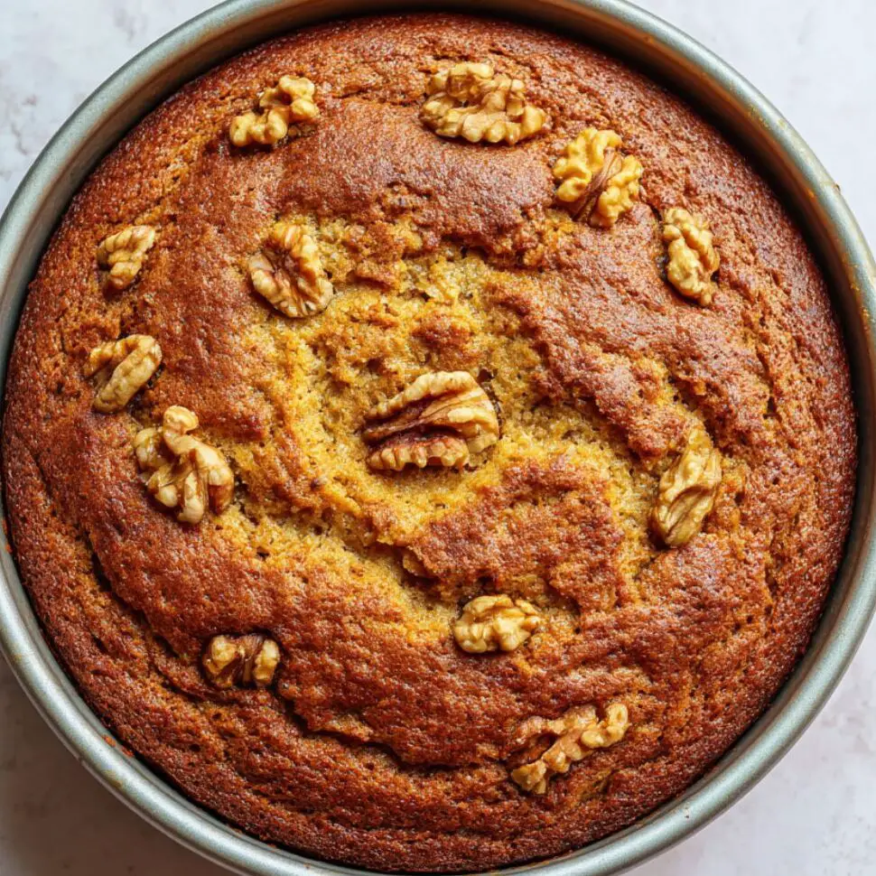 Golden-brown date and walnut cake still in its baking pan, just out of the oven on a white countertop.

