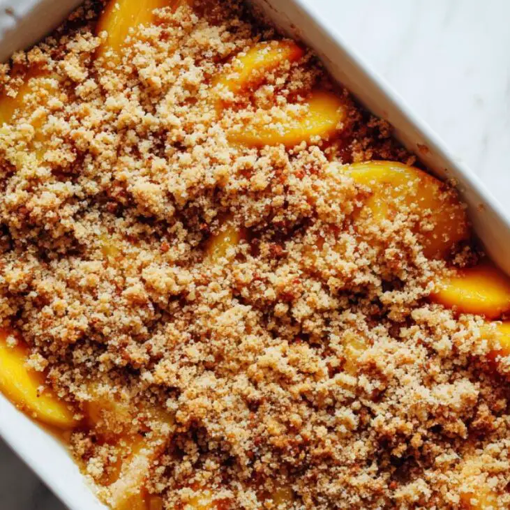 Crumb topping spread over peaches in pan, ready to bake.