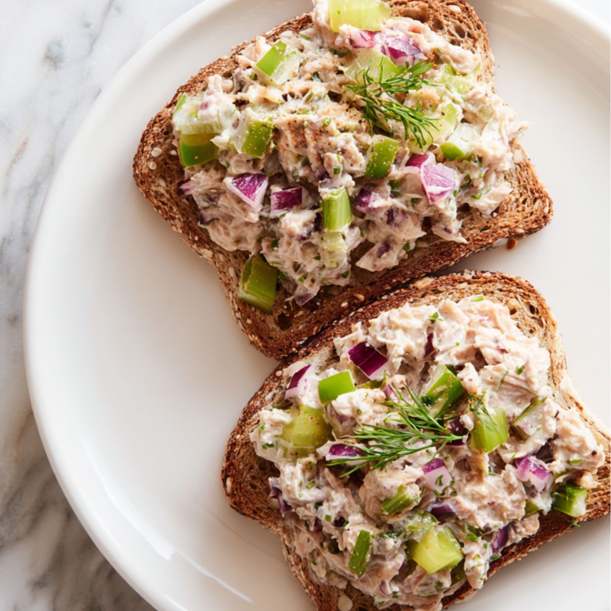 Overhead view of homemade tuna salad toast recipe with chunky filling on toasted multigrain bread