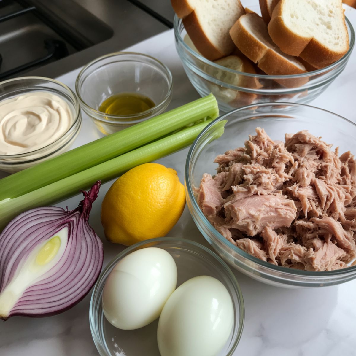 Flat lay of tuna salad ingredients including tuna, celery, lemon, red onion, boiled eggs, and bread