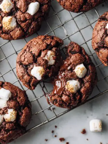 Freshly baked hot cocoa cookies recipe with melted chocolate and marshmallows on a cooling rack