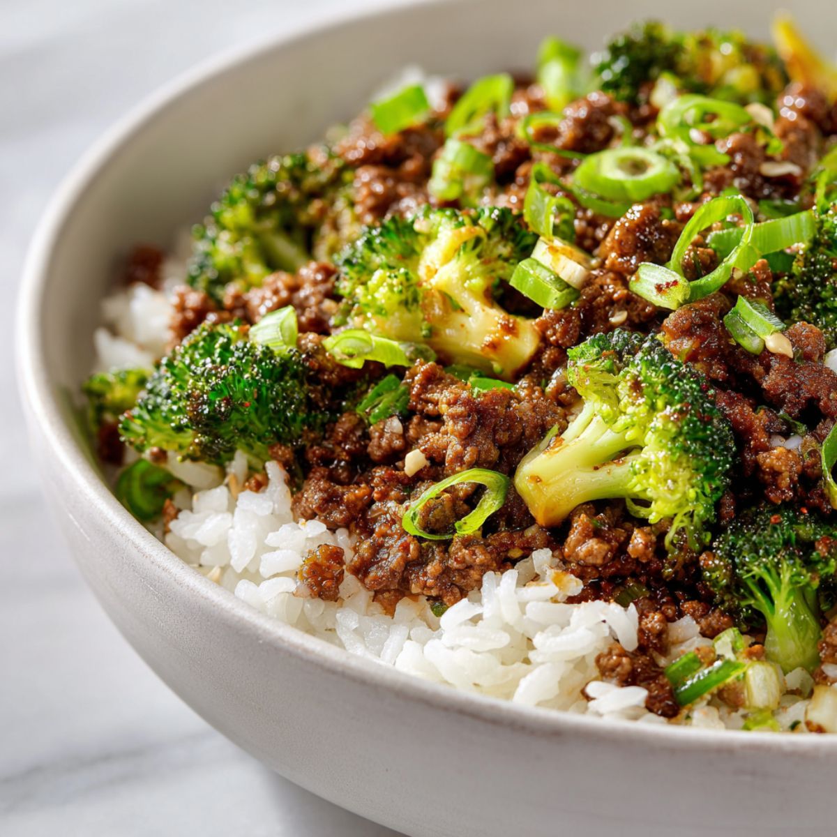 Overhead shot of a homemade beef bowls recipe with ground beef, rice, and vegetables served in a white bowl on a white kitchen counter.