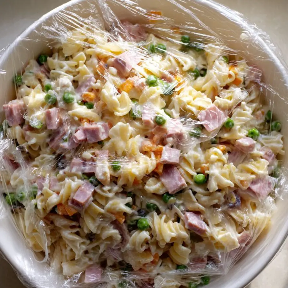 Ham and cheese pasta salad covered with plastic wrap in a refrigerator