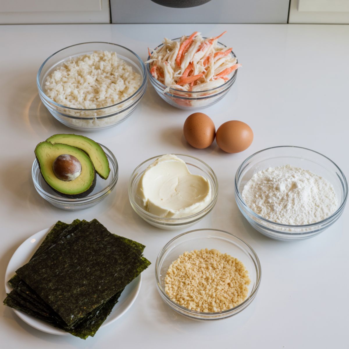 Ingredients for making crispy crab rolls including crab, avocado, rice, nori, eggs, and panko.
