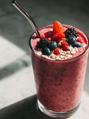 Homemade Greek yogurt smoothie recipe in a glass with berries and banana on a marble counter