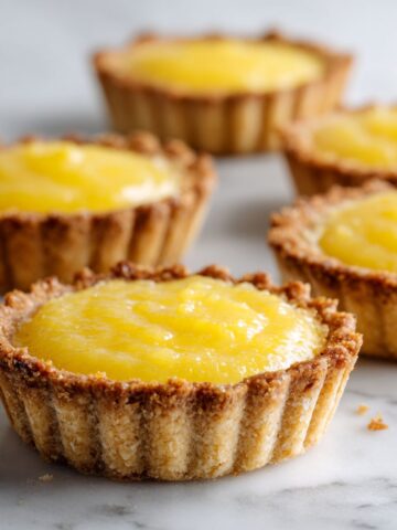 Homemade mini lemon tarts recipe filled with lemon curd, slightly rustic look, on a white kitchen counter, overhead view.