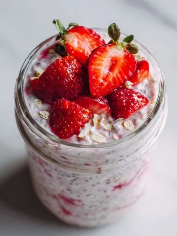 Homemade strawberry chia overnight oats recipe served in a glass jar on a white kitchen counter, topped with fresh strawberries and chia seeds.