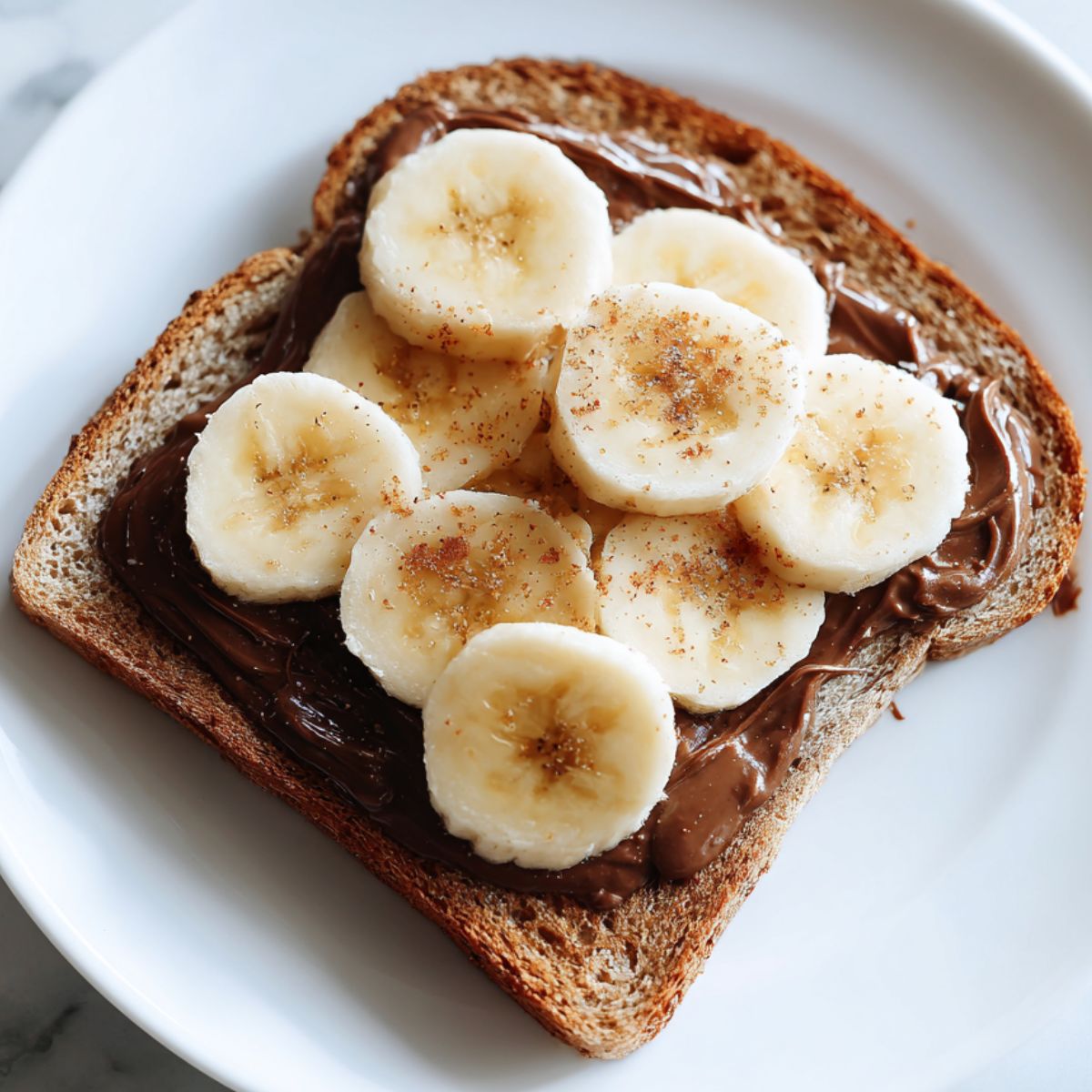 Homemade Nutella and banana toast recipe stacked on a white plate taken from above

