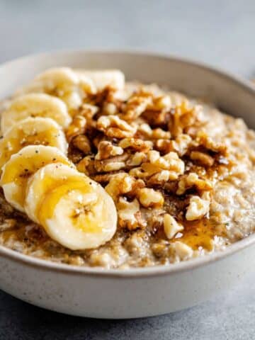 Homemade banana nut oatmeal recipe topped with banana slices, walnuts, and honey on a white kitchen counter, overhead view.