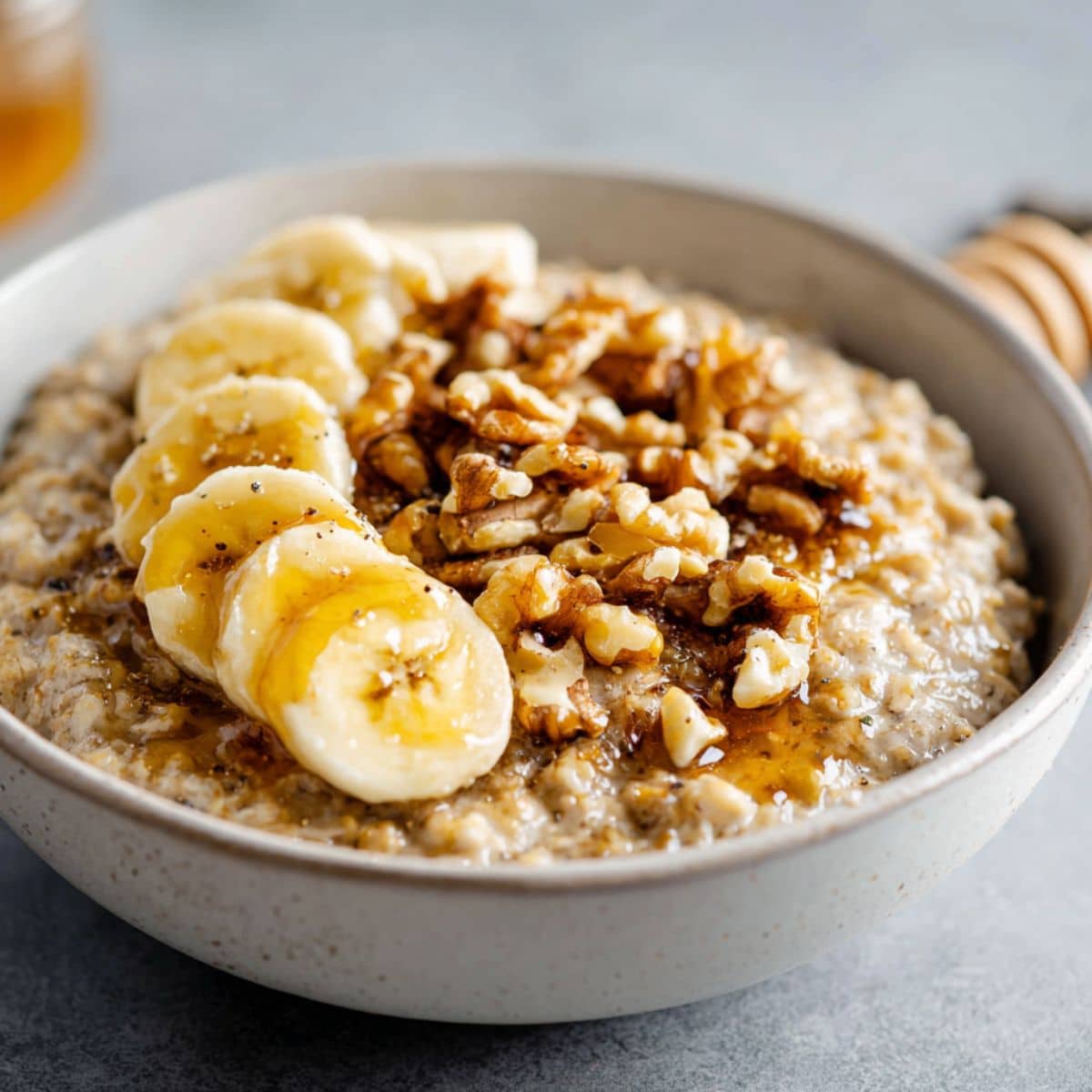 Homemade banana nut oatmeal recipe topped with banana slices, walnuts, and honey on a white kitchen counter, overhead view.