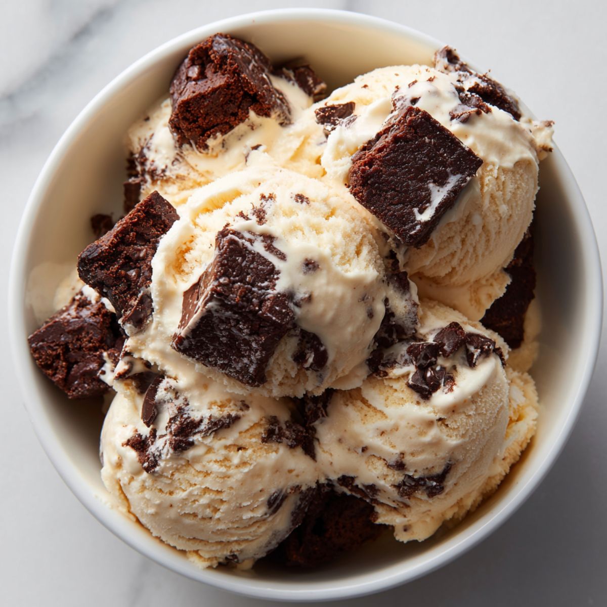 Homemade brownie chunk ice cream recipe with vanilla base and fudgy brownie pieces on white marble counter