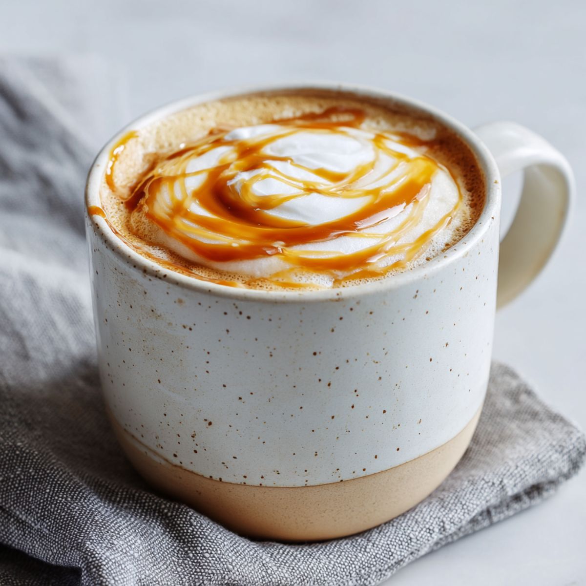 Homemade caramel latte recipe with milk foam and caramel drizzle on a white kitchen counter.