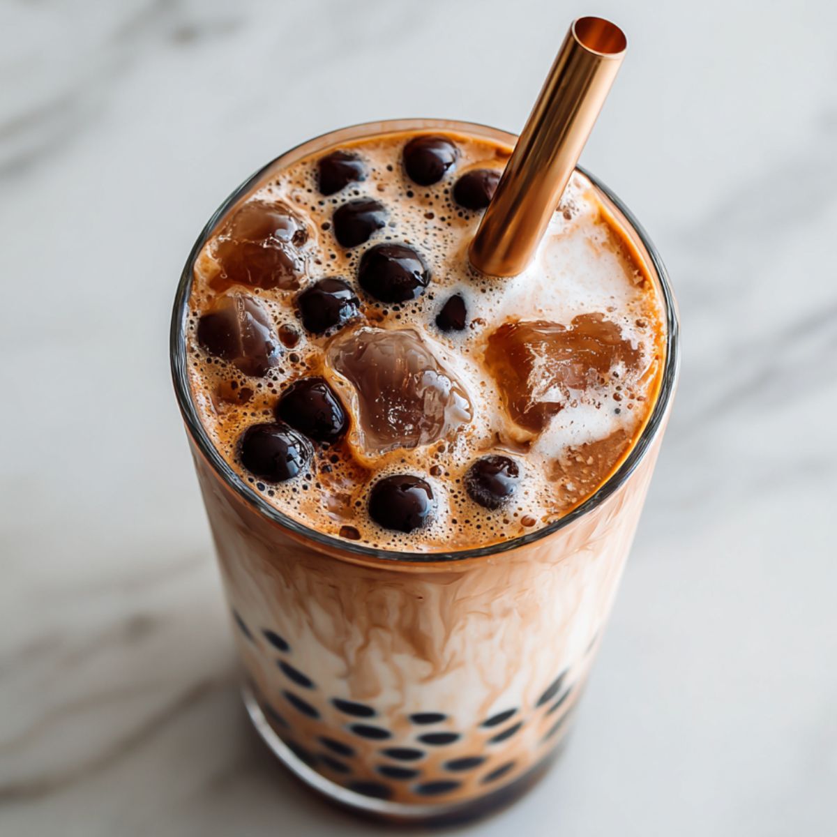 Homemade chocolate bubble tea recipe with tapioca pearls served in a tall glass on a white marble counter.