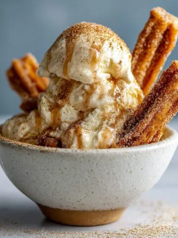 Homemade churro ice cream recipe served in a bowl with churro pieces and cinnamon sugar, shot overhead on a white kitchen counter.
