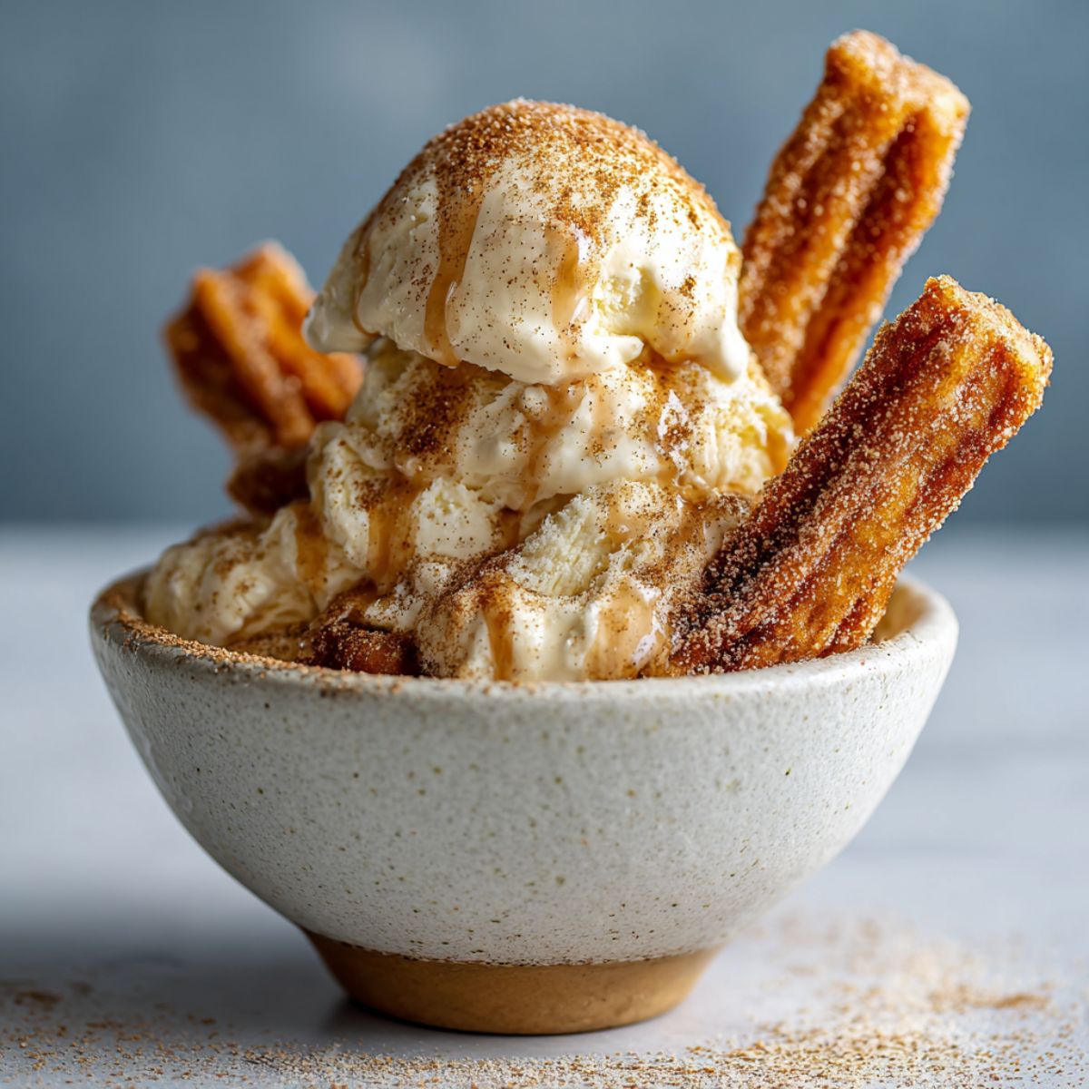 Homemade churro ice cream recipe served in a bowl with churro pieces and cinnamon sugar, shot overhead on a white kitchen counter.