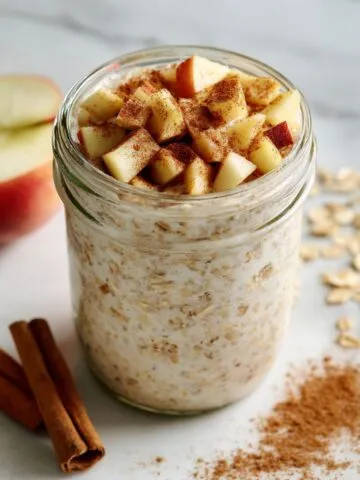 Homemade cinnamon apple overnight oats recipe in a glass jar on a white marble kitchen counter, photographed from above.