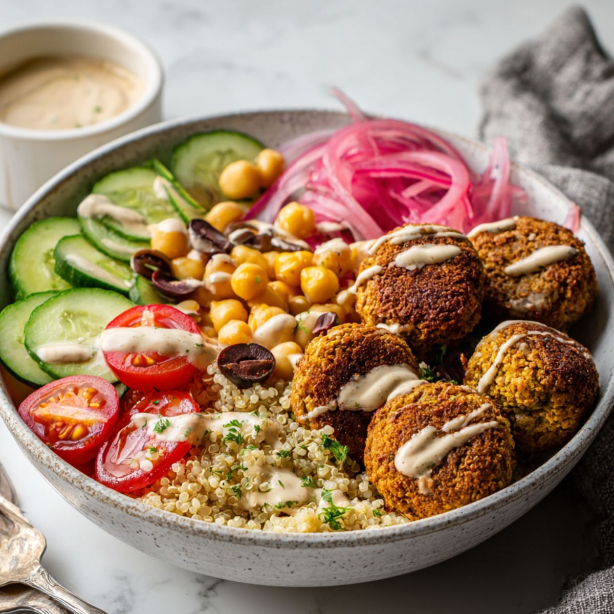 Overhead photo of a Falafel Bowls Recipe with quinoa, crispy falafel, fresh vegetables, and tahini drizzle on a white kitchen counter.