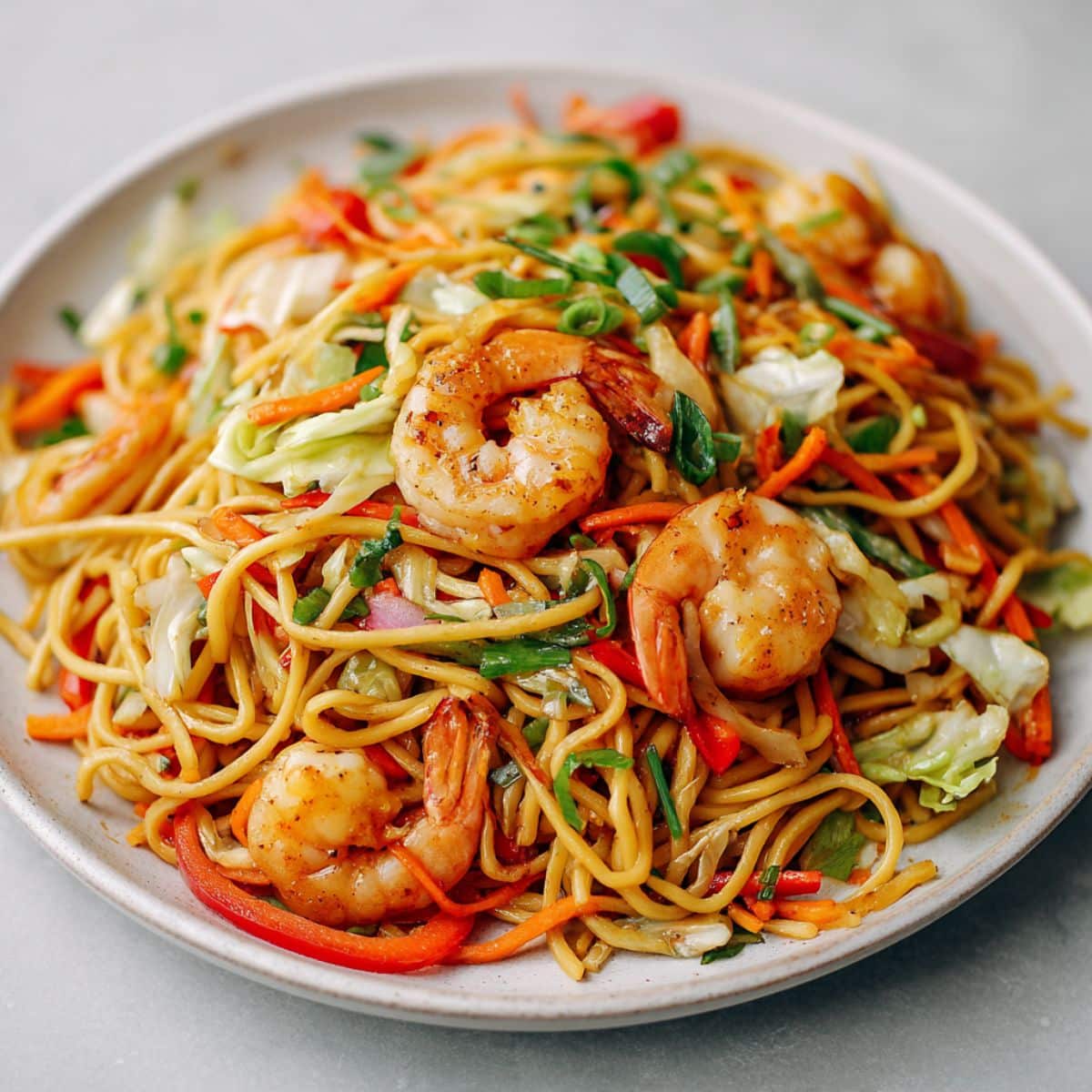 Overhead view of homemade shrimp lo mein recipe with shrimp and vegetables on a white kitchen counter, casually plated in a natural homemade style.