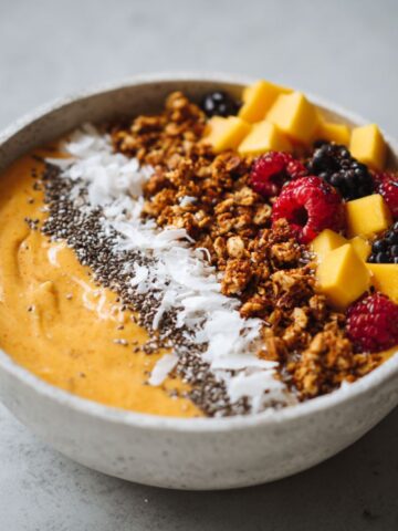 Homemade papaya smoothie bowl recipe topped with granola, chia seeds, mango, and berries on a white kitchen counter.