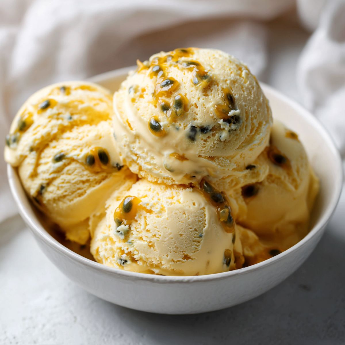 Homemade passionfruit ice cream recipe in a bowl with visible seeds on a white kitchen counter