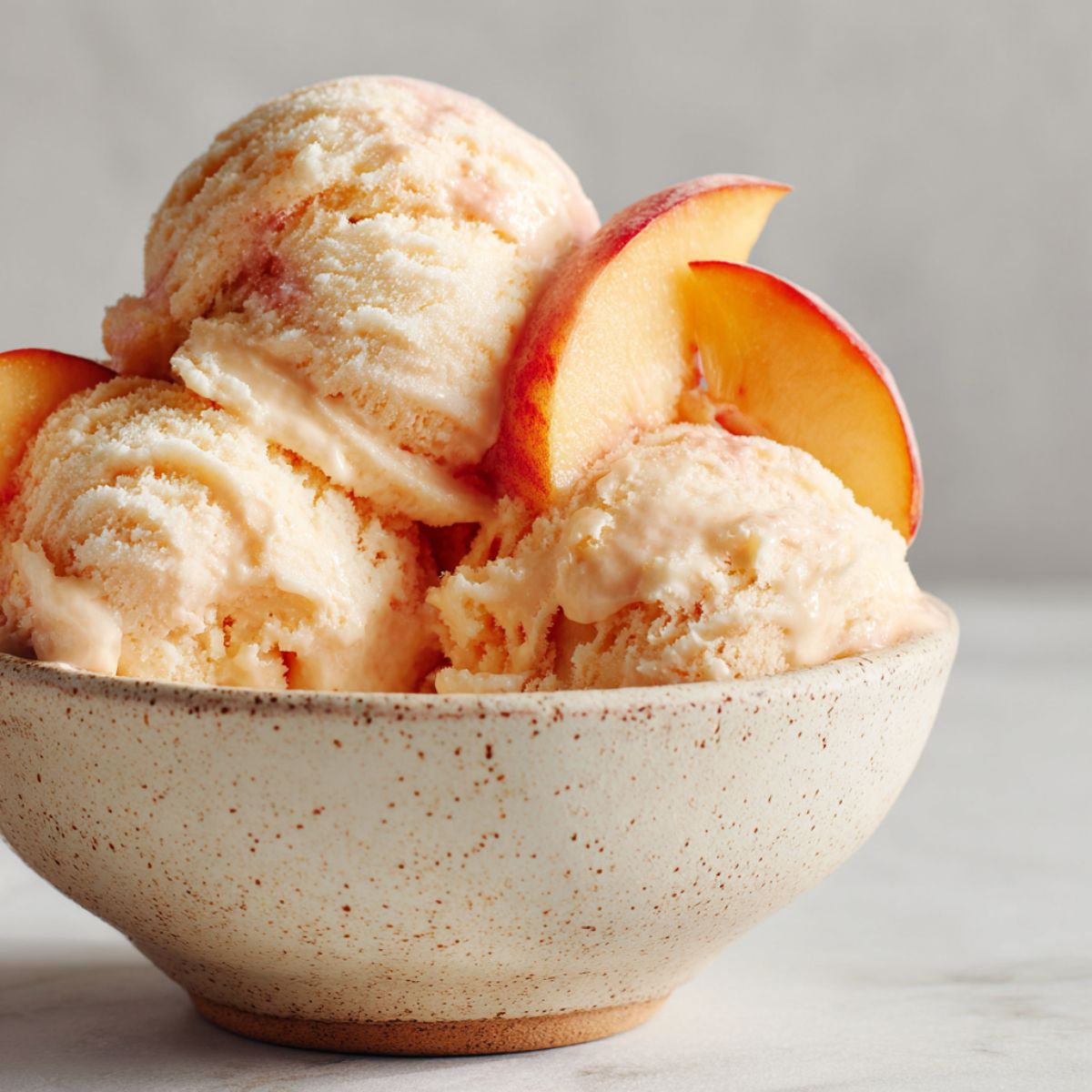 Bowl of homemade peach ice cream recipe with peach slices on a white marble counter