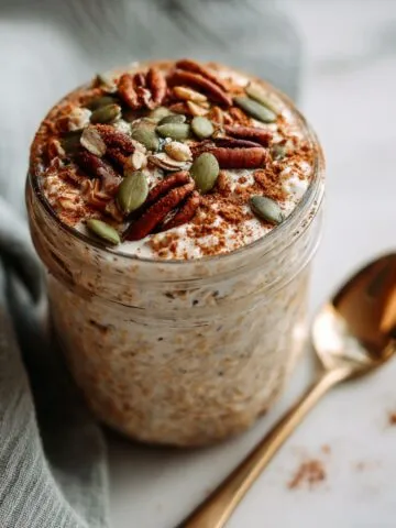 Overhead shot of pumpkin spice overnight oats recipe in a jar on a white marble counter, topped with pecans and pumpkin seeds, homemade style.