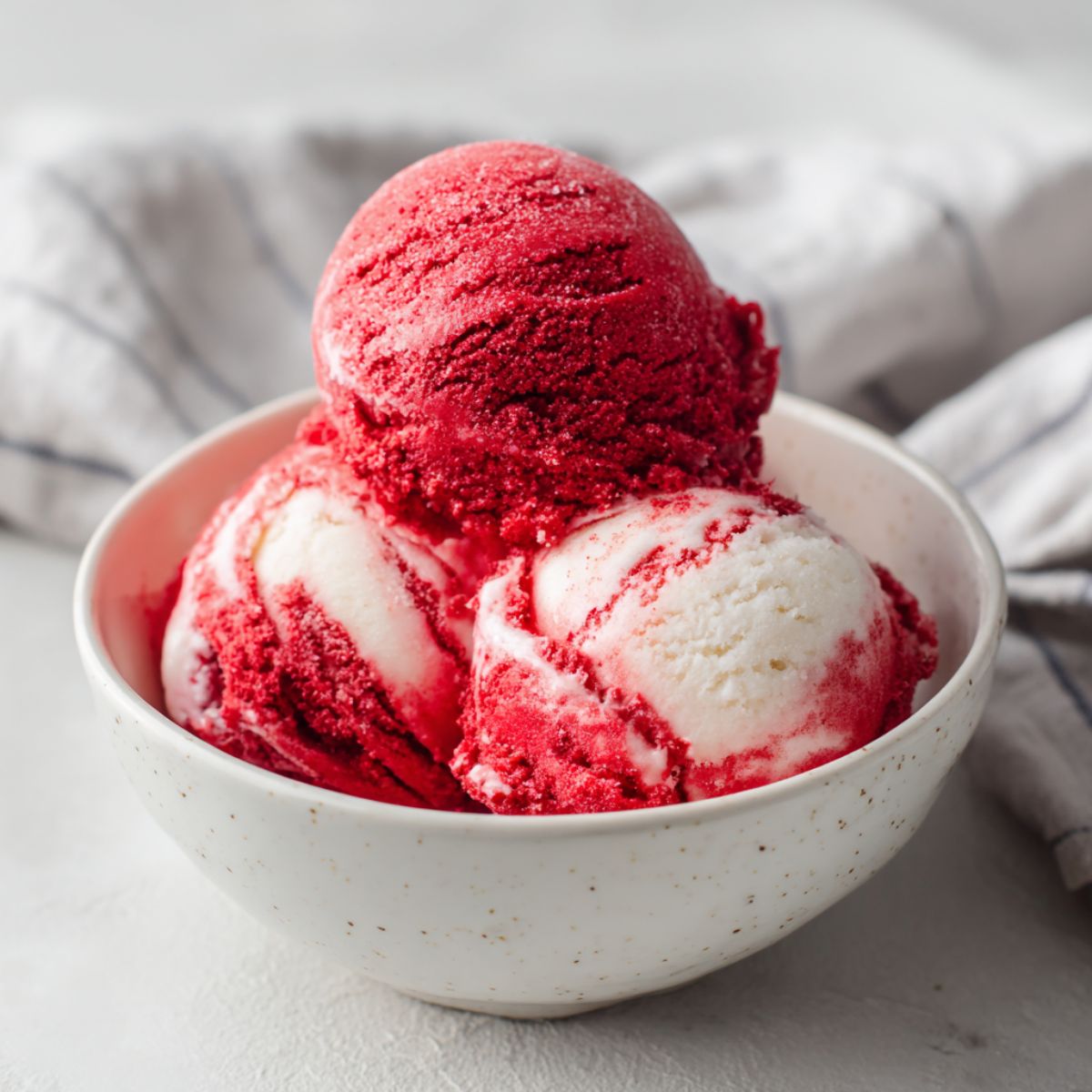 Homemade red velvet ice cream recipe scoops in a bowl on a white counter.