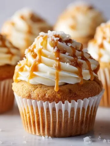 Overhead shot of homemade salted caramel cupcakes recipe with caramel drizzle and sea salt on a white kitchen counter, casual homemade style.