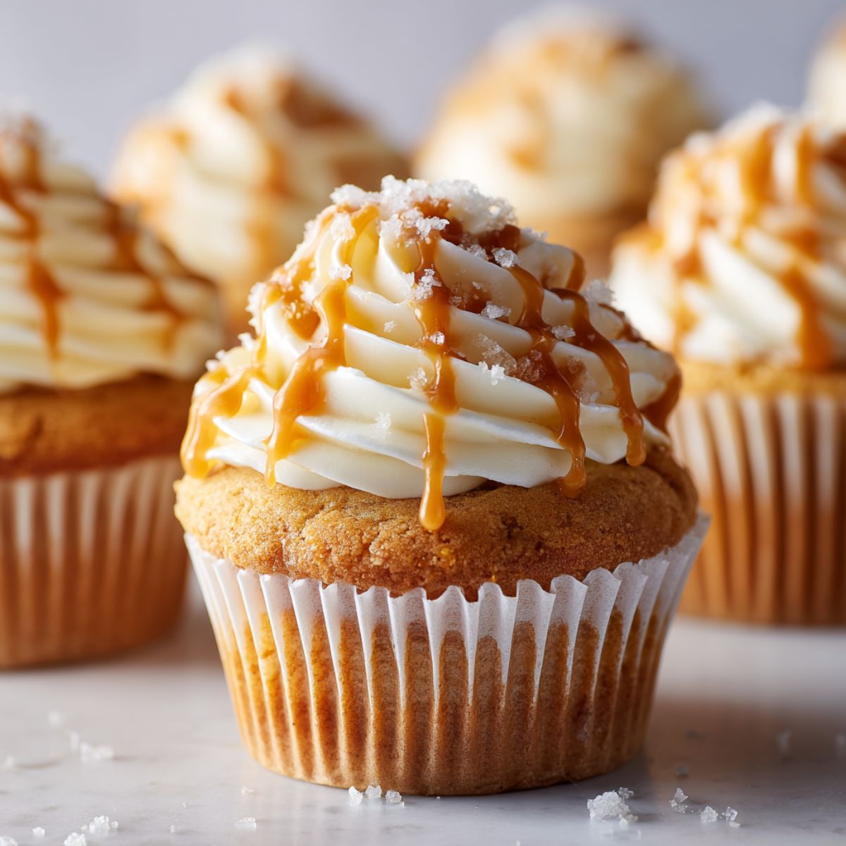 Overhead shot of homemade salted caramel cupcakes recipe with caramel drizzle and sea salt on a white kitchen counter, casual homemade style.
