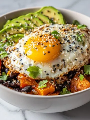 Homemade sweet potato breakfast bowl recipe with avocado, fried egg, black beans, and feta on a white kitchen counter, photographed from above.