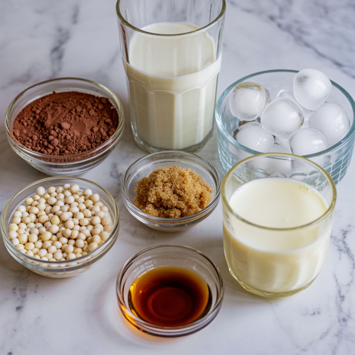 Ingredients for homemade chocolate bubble tea displayed on a white marble counter.