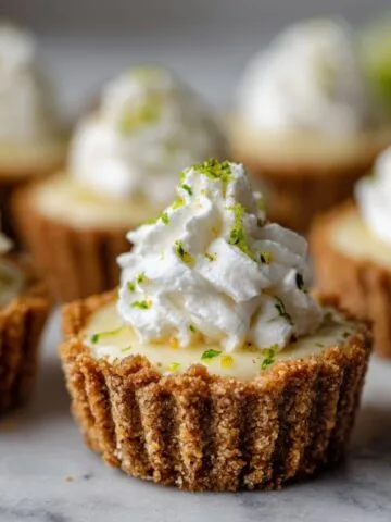 Overhead photo of homemade mini key lime pies recipe with graham cracker crust, whipped cream, and lime zest on a white kitchen counter.