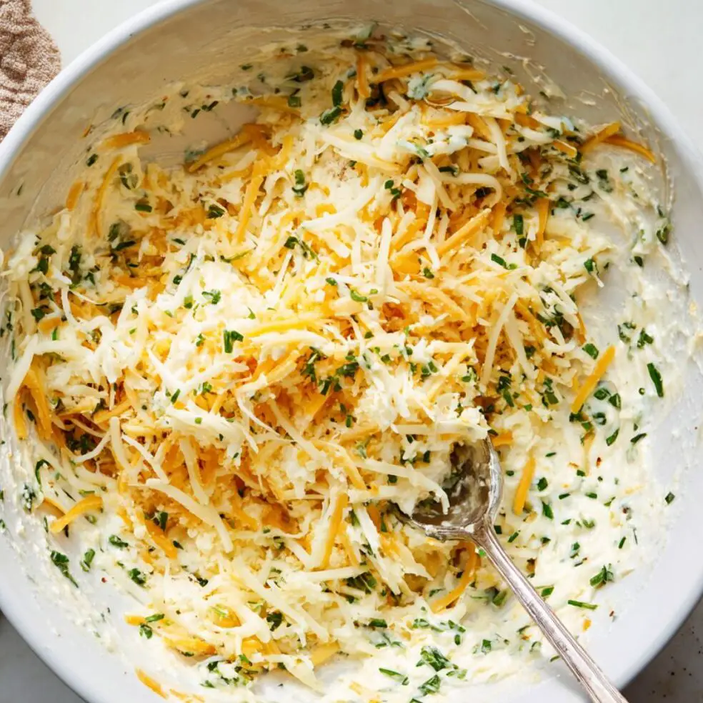 Cheese mixture in a bowl with herbs and garlic being stirred together.

