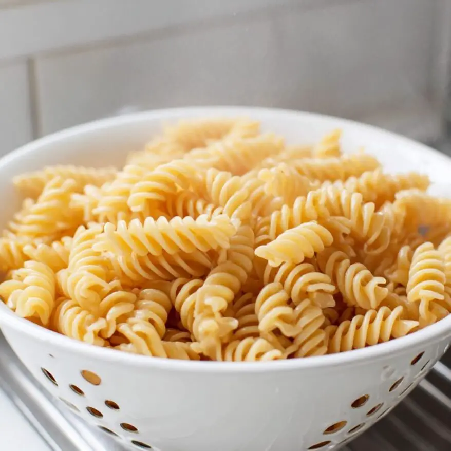 Freshly cooked rotini pasta draining in a white colander on a kitchen counter