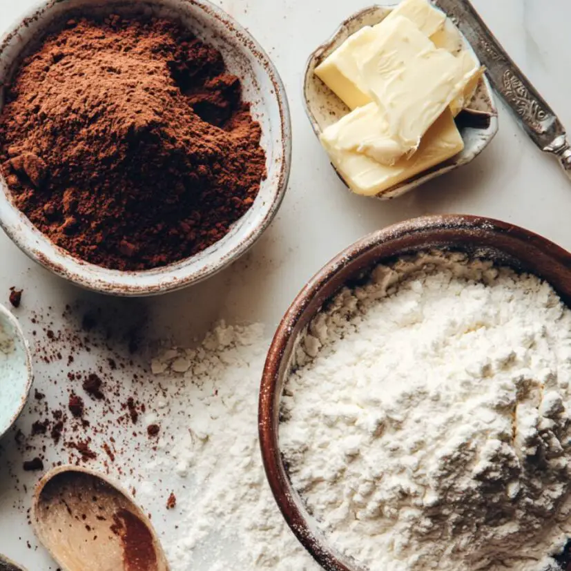 Cookie prep setup with bowls, flour, cocoa, and butter on a kitchen counter.